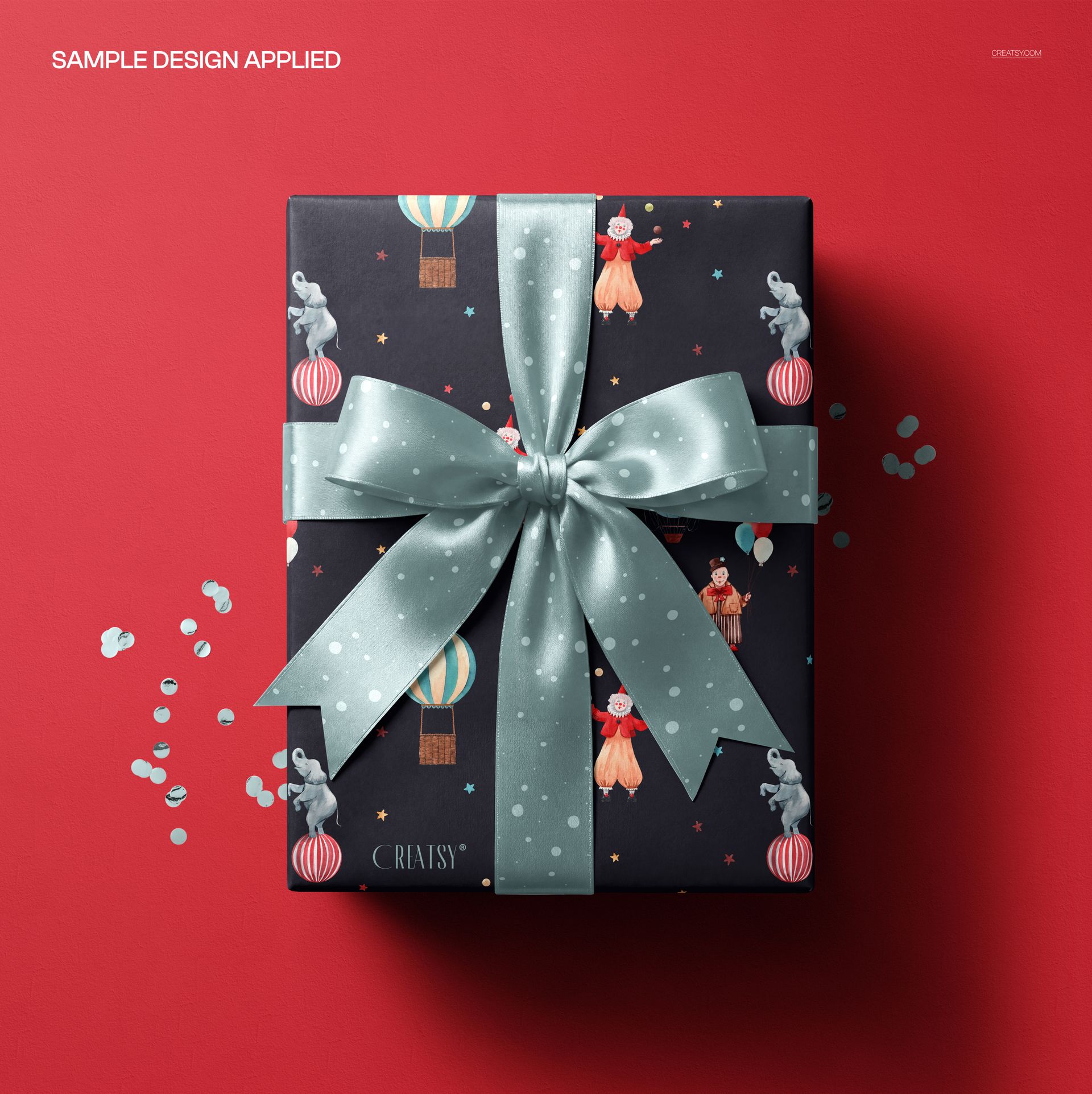 Top view of a mockup featuring a gift box wrapped in whimsical paper with clowns and balloons, finished with a bow.