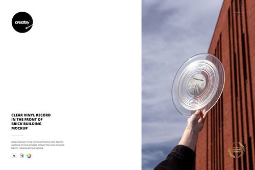 Hand holding a transparent vinyl record mockup with visible grooves, positioned before a red brick wall outdoors.