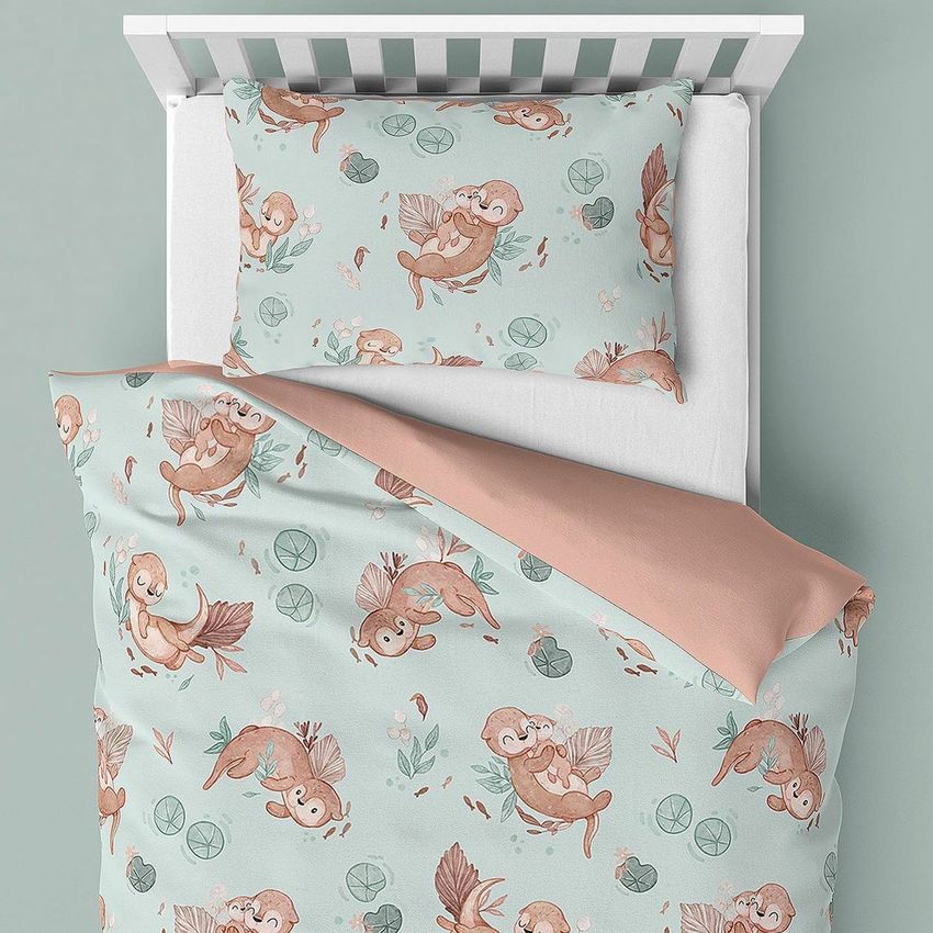 Kids bedding mockup showing a crib with a pillow and duvet featuring playful otter illustrations on a light blue background.