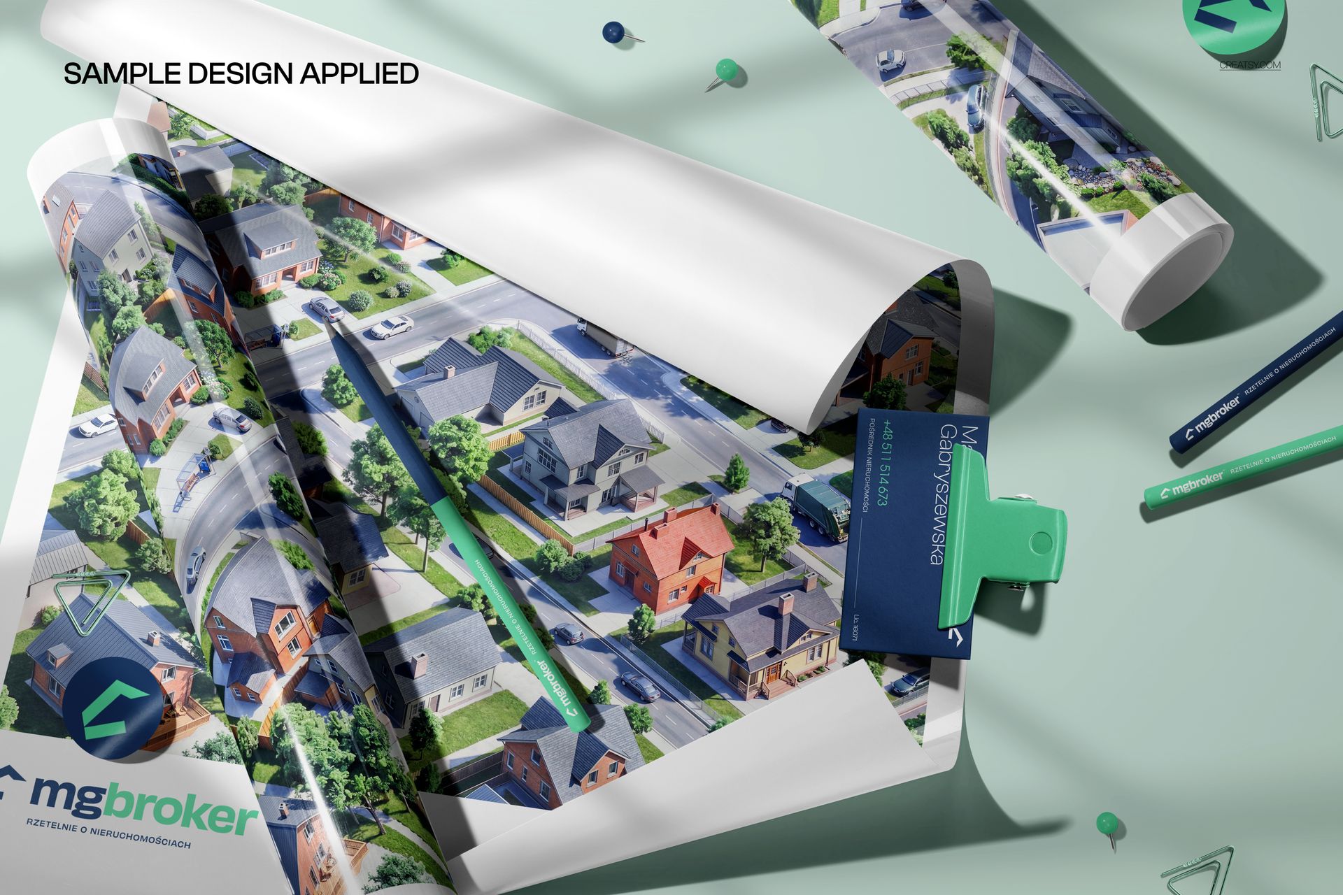 Glossy poster mockup with a rolled map design, surrounded by stationery items like pens and business cards on a light surface.