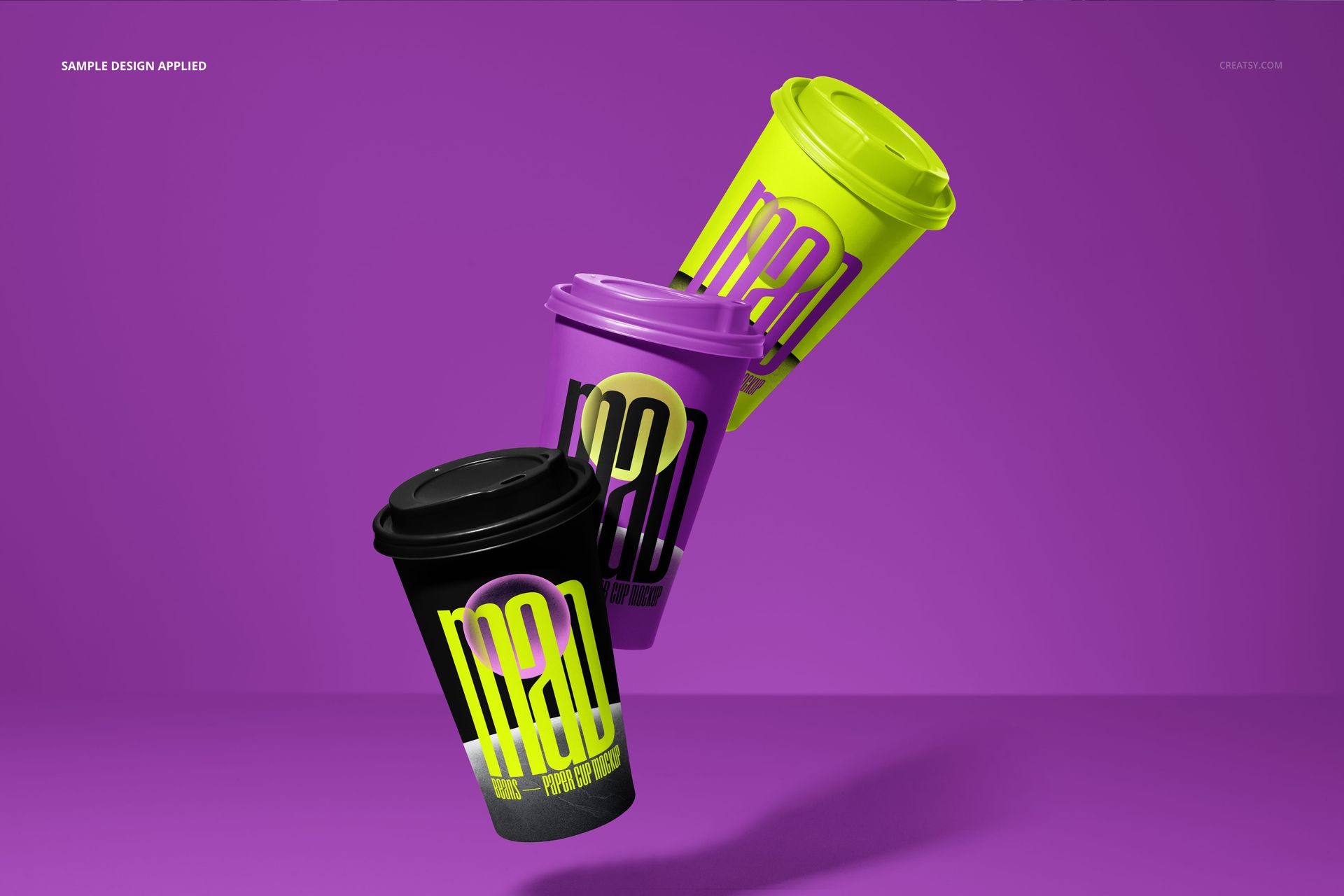 PSD mockup featuring trio of paper cups in vibrant black, purple, and yellow, displayed on a plain purple backdrop.