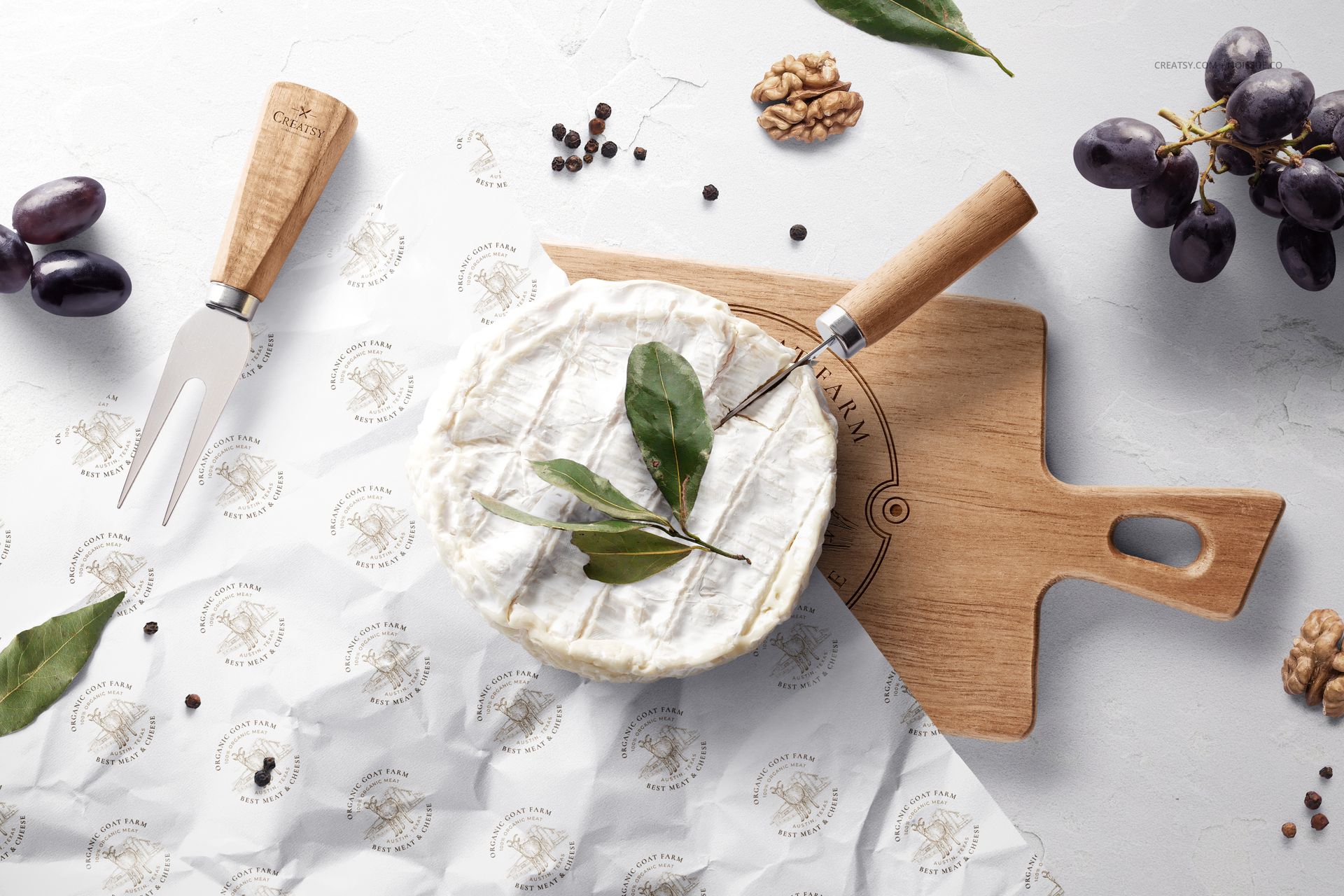 PSD mockup scene featuring camembert cheese, printed wrapping paper, wooden board, fork, grapes, and nuts, top perspective.