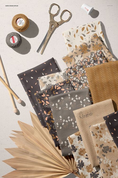 Top view of patterned jersey fabrics, crochet threads, scissors, and dried palm leaf displayed together in a PSD mockup scene.