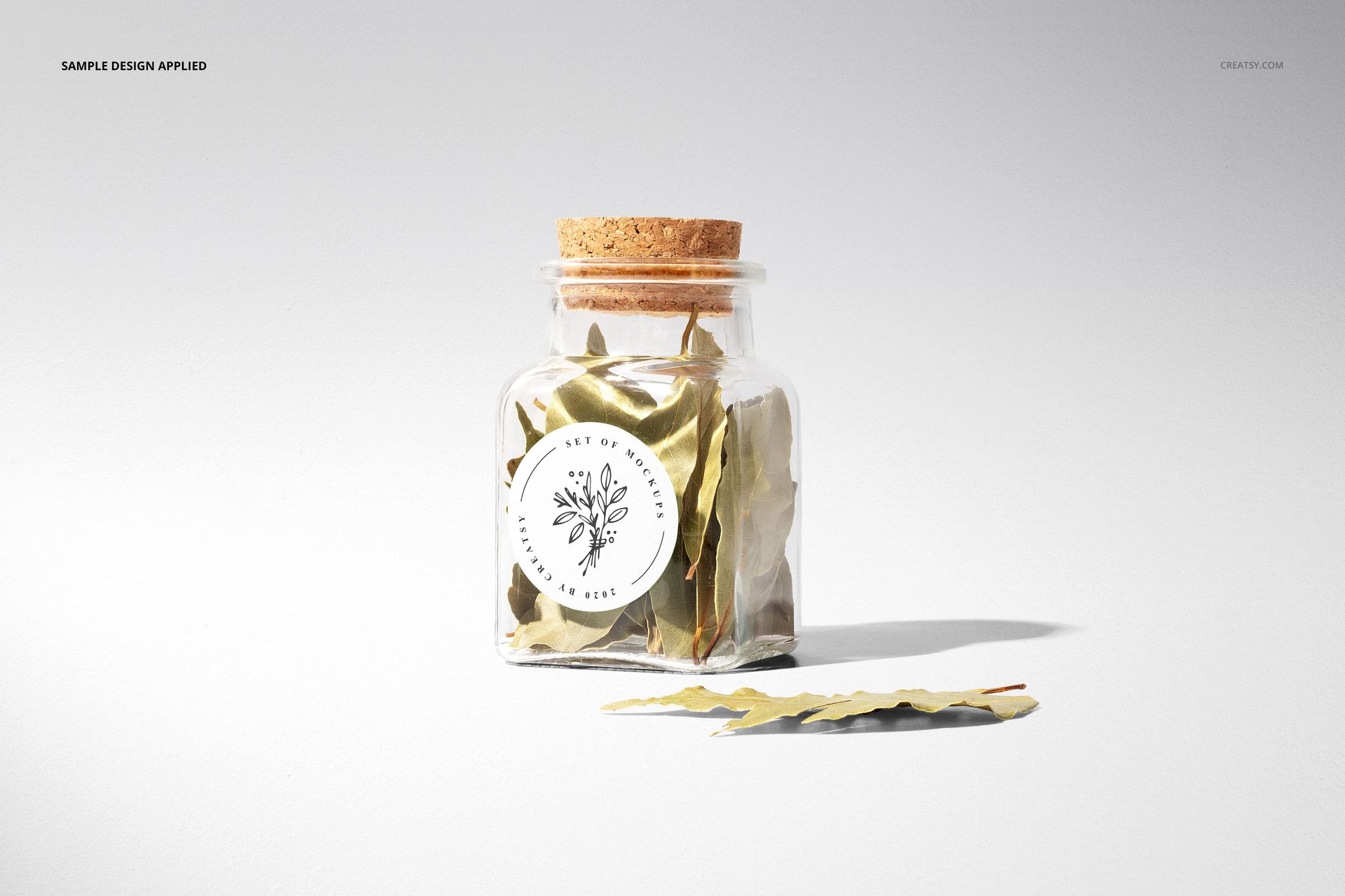 Mockup of a clear spice jar with cork stopper, round label on front, filled with dried leaves, minimalist setting.