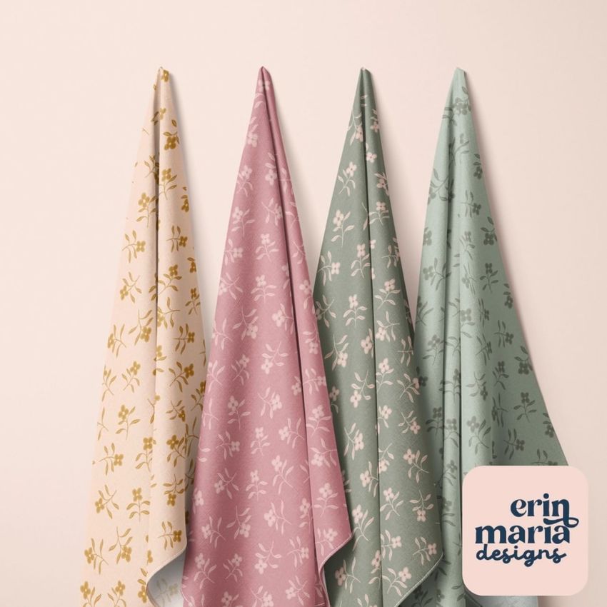 Hanging fabrics mockup showing four cloths with delicate floral patterns in cream, pink, green, and sage colors on a light wall.