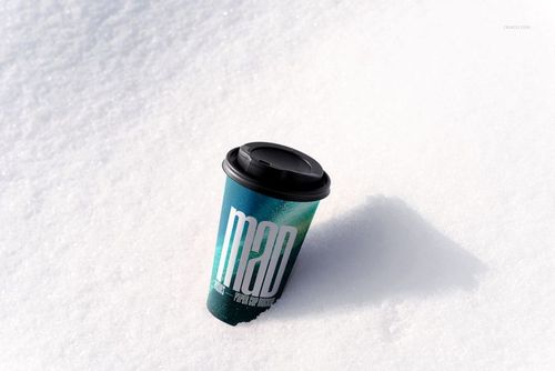 Winter-themed PSD mockup of a paper cup with a black lid and modern blue pattern, positioned on snowy ground.