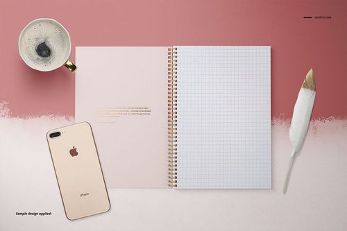 Open A4 notebook mockup with spiral binding and grid pages, placed beside a coffee cup, phone, and white feather.