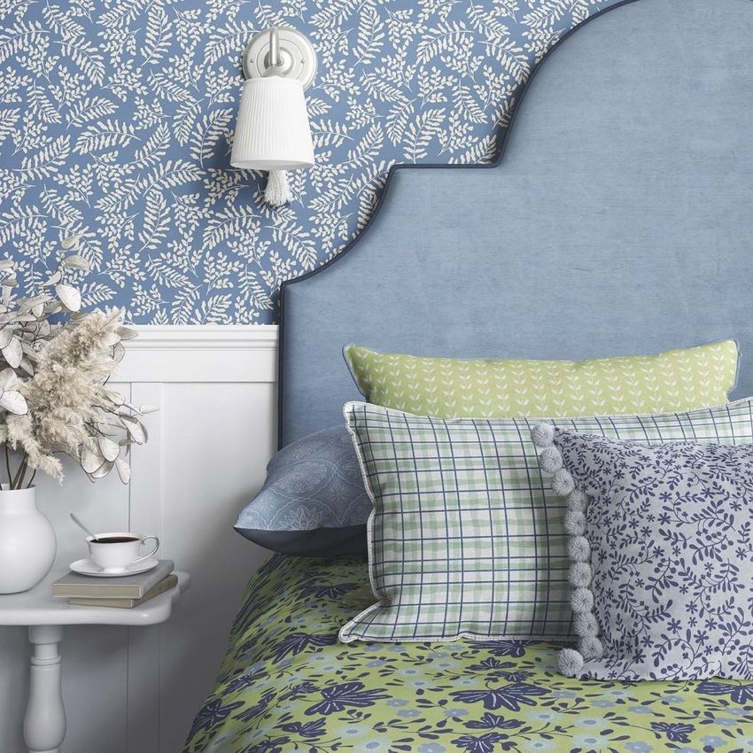 Bedroom mockup showing a blue upholstered headboard, patterned pillows, and blue floral wallpaper above white paneling.