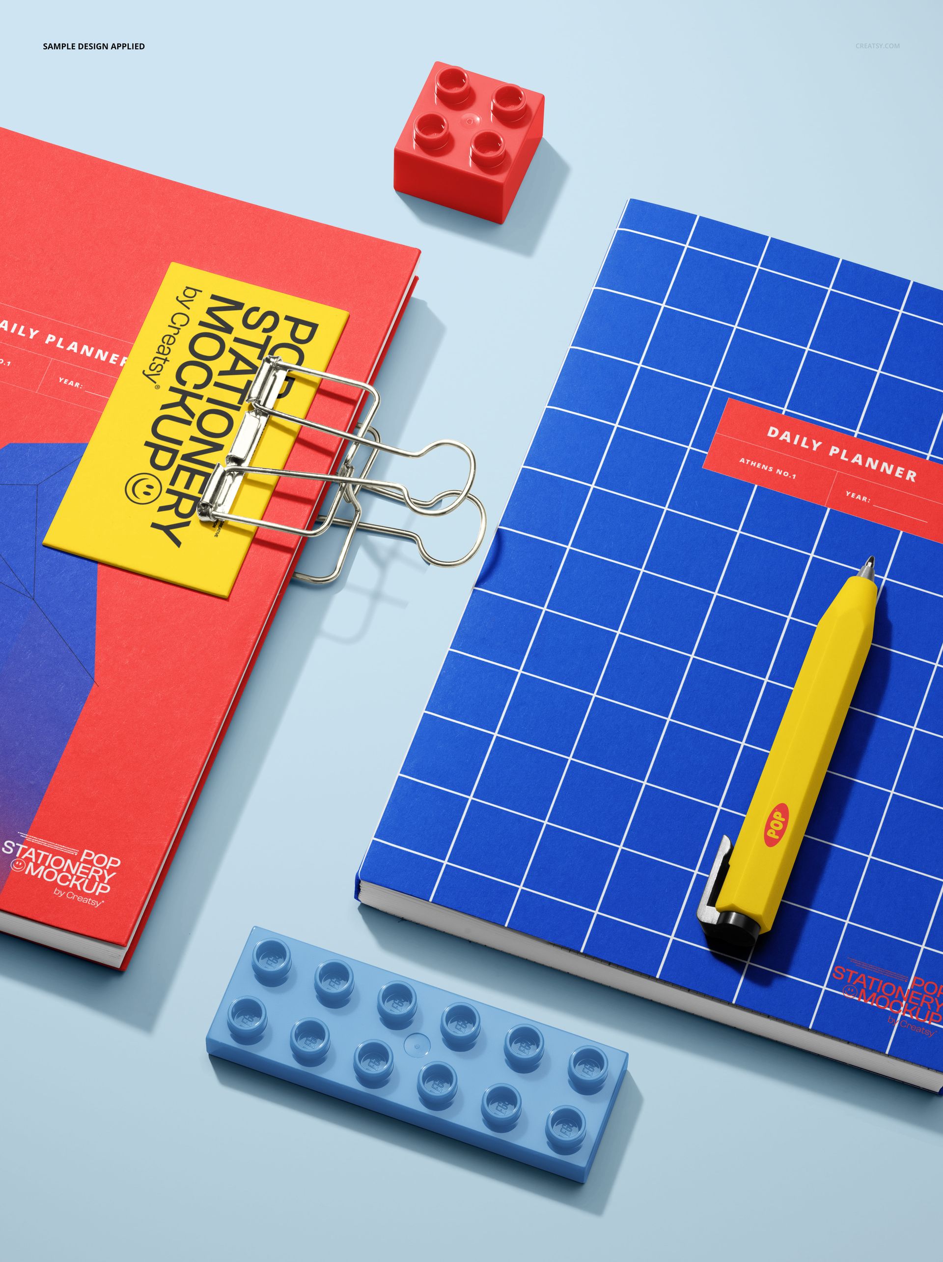PSD mockup showing daily planners in red and blue, with colorful plastic building blocks and office accessories on a blue background.